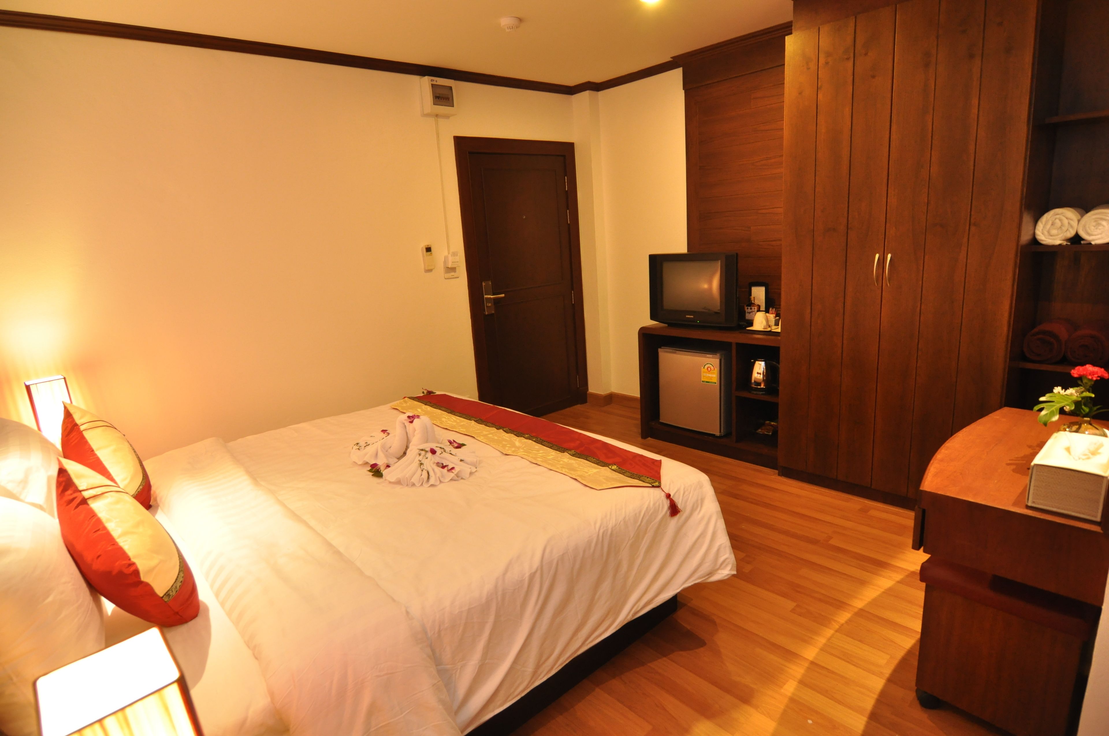 A hotel room with a bed, a television, a minibar, and a wardrobe.