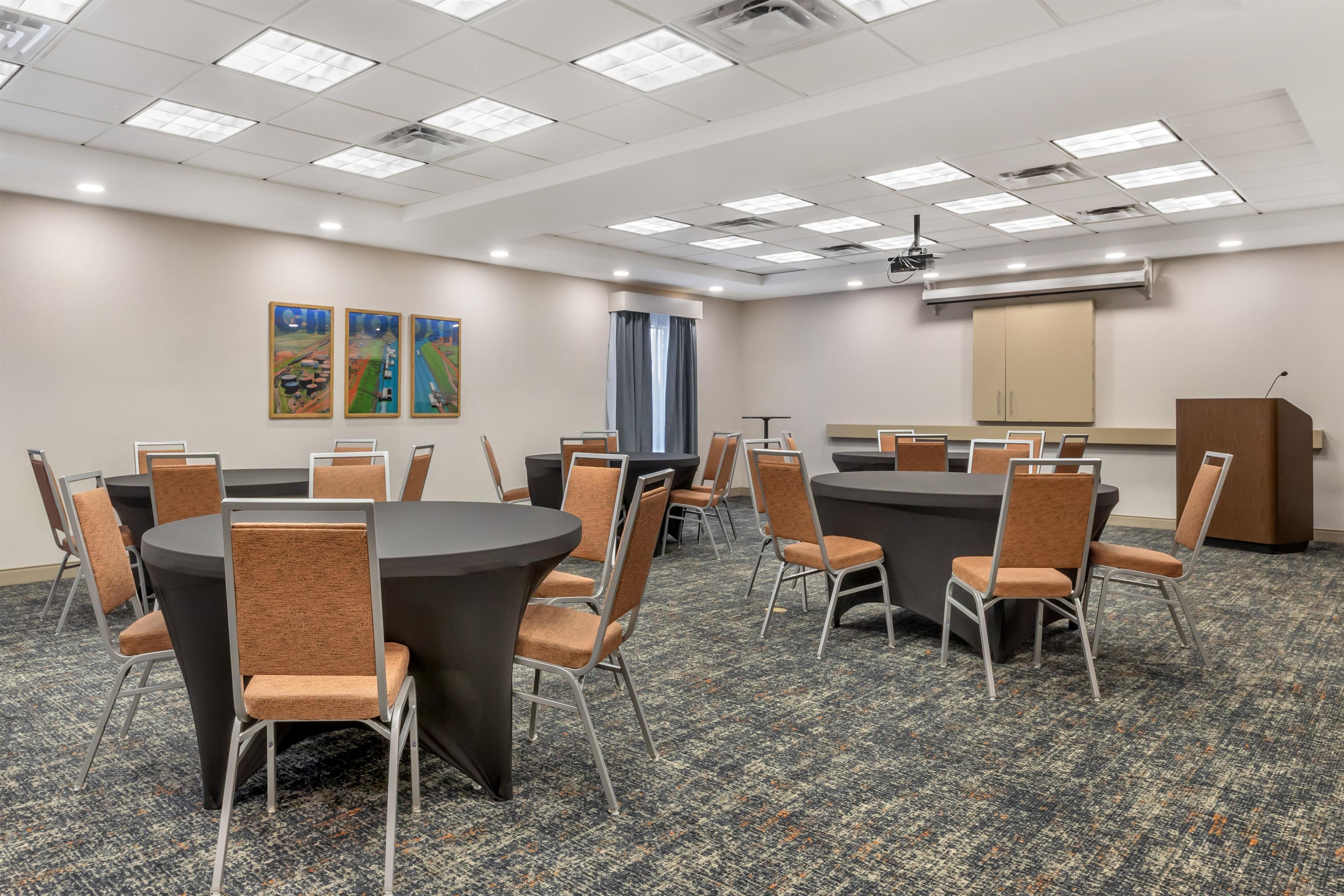 A conference room with round tables and chairs, a podium, and a projector screen.