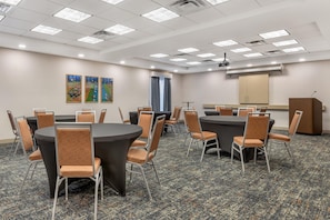 A conference room with round tables and chairs, a podium, and a projector screen. - Hampton Inn & Suites Tulsa/Catoosa (Catoosa)
