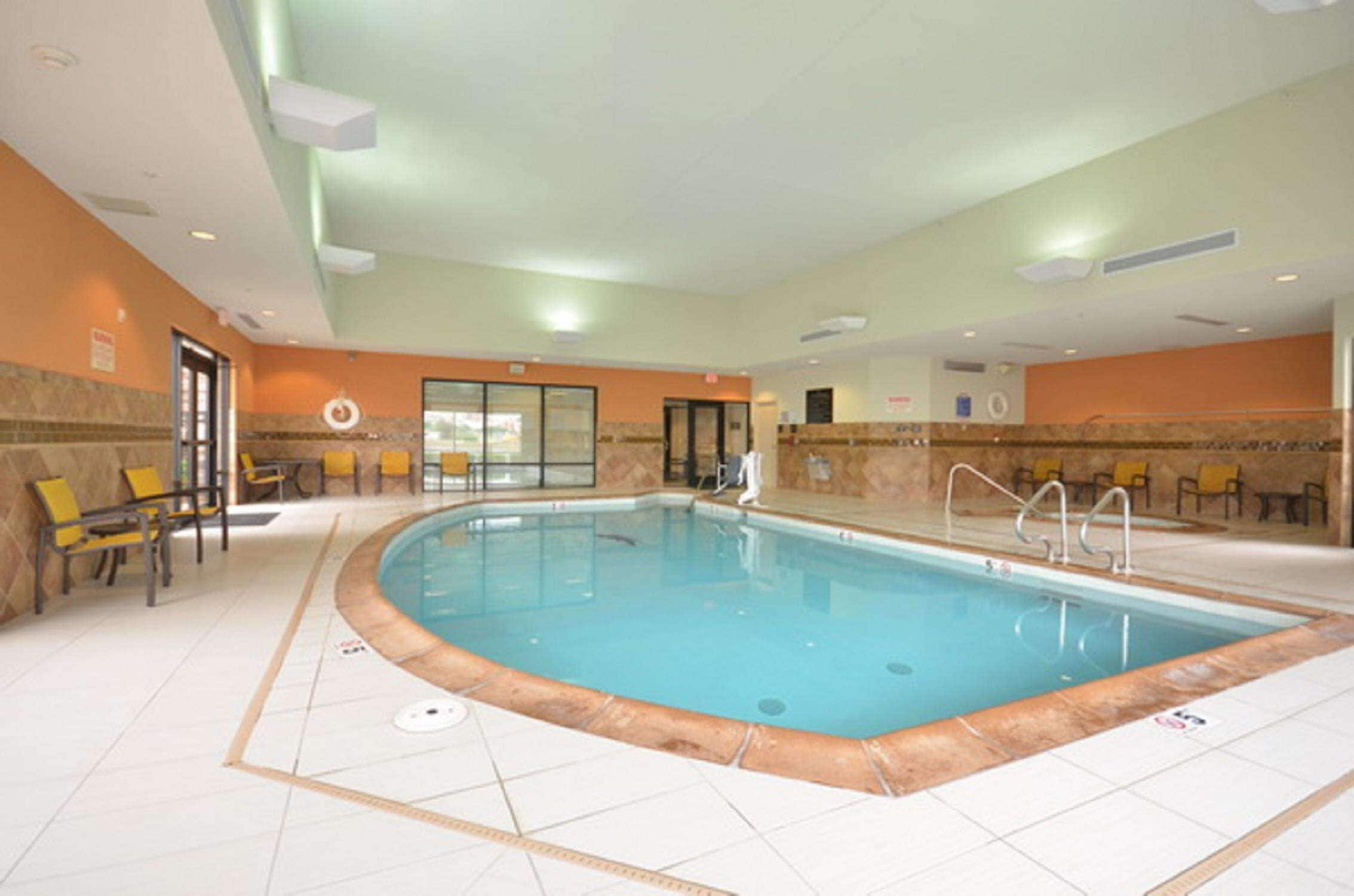 Una piscina interior con suelo de baldosas, sillas amarillas y acceso mediante puerta de vidrio.