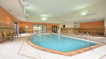 Una piscina interior con suelo de baldosas, sillas amarillas y acceso mediante puerta de vidrio.