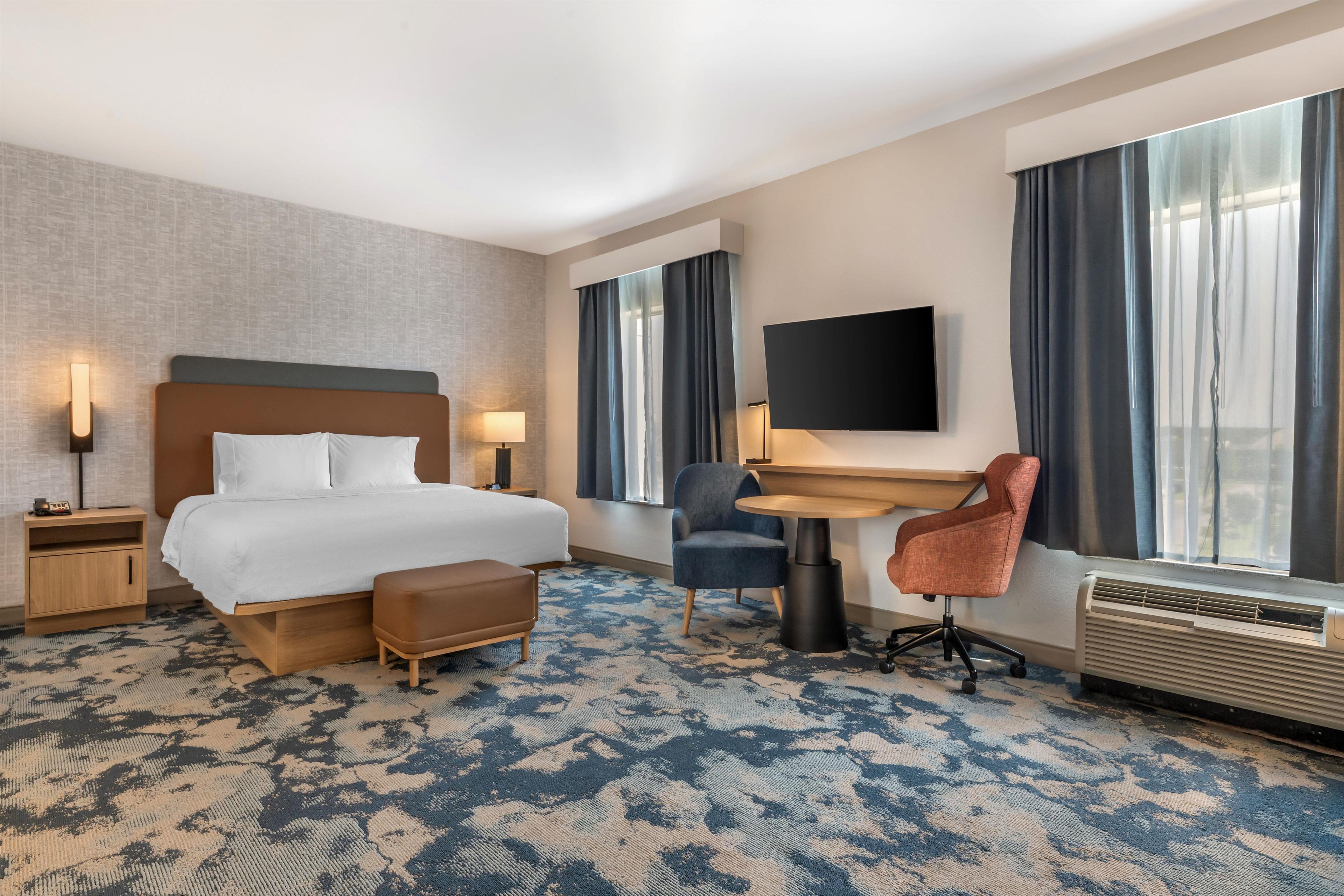 A hotel room with a bed, desk, chair, and a flat-screen TV.