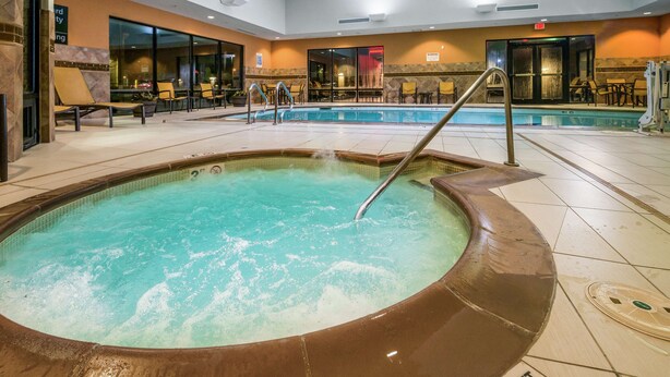 Un bain à remous avec une piscine adjacente, entouré de chaises longues et d’un espace détente avec des tables.