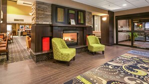 Un hall d’entrée avec une cheminée, deux fauteuils verts, un tapis à motifs et un espace d’accueil avec des chaises et un comptoir.