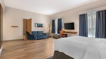 A hotel room with a bed, a sofa, a desk, a TV, and a painting on the wall.