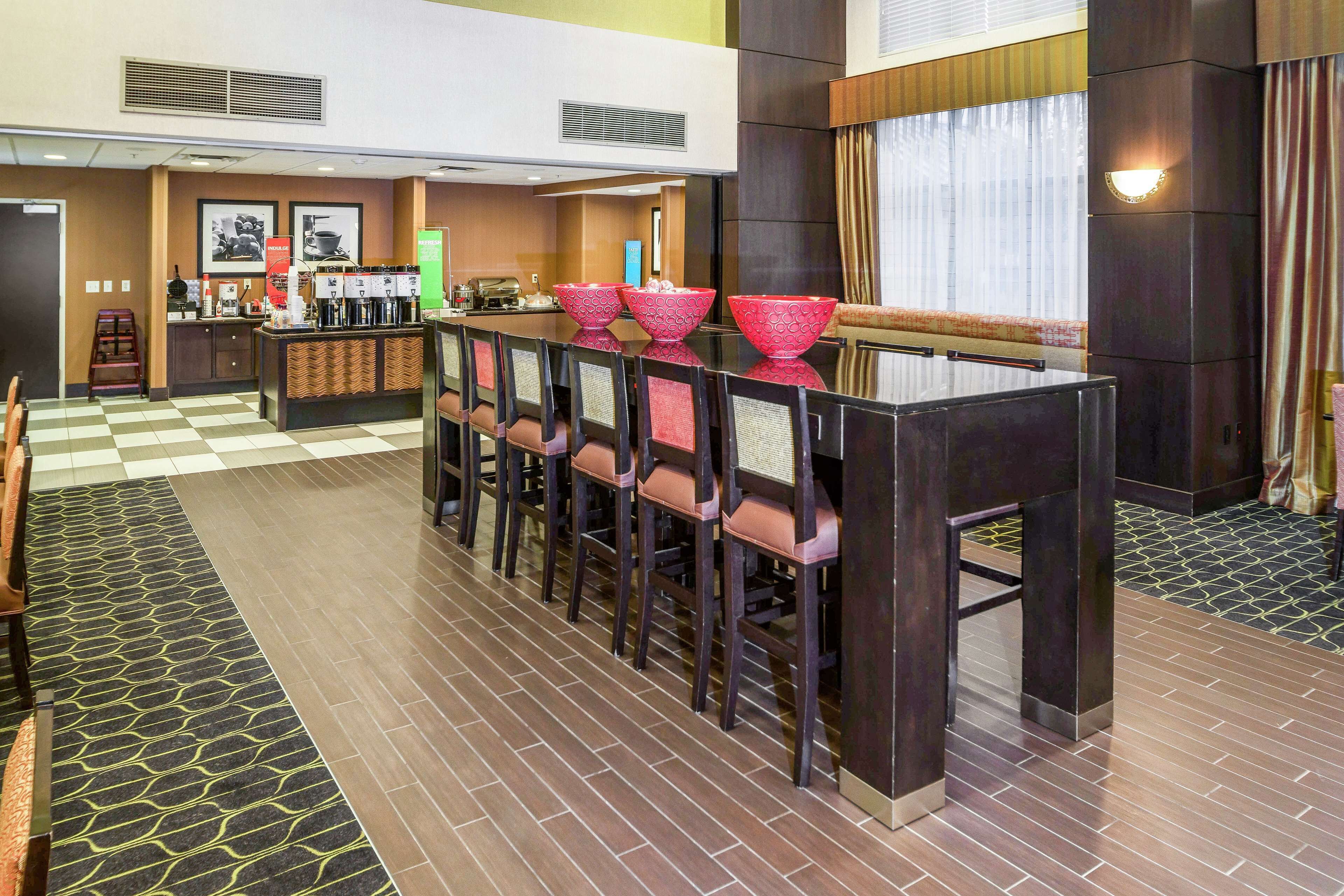 Un vestíbulo de hotel con piso a cuadros, una recepción y una zona de bar con taburetes rojos.