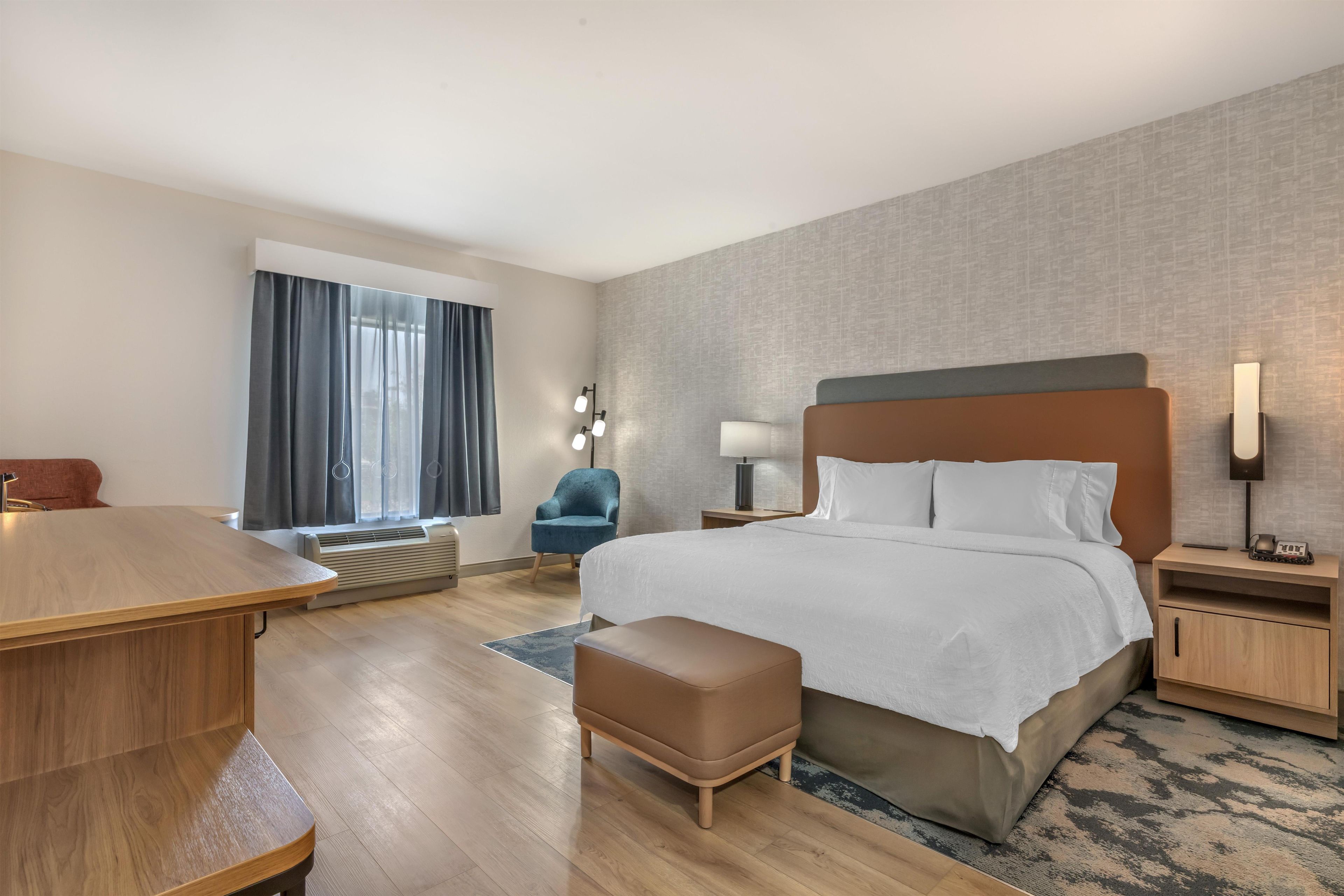 Una habitación de hotel con cama, escritorio, silla, mesita de noche y lámpara.