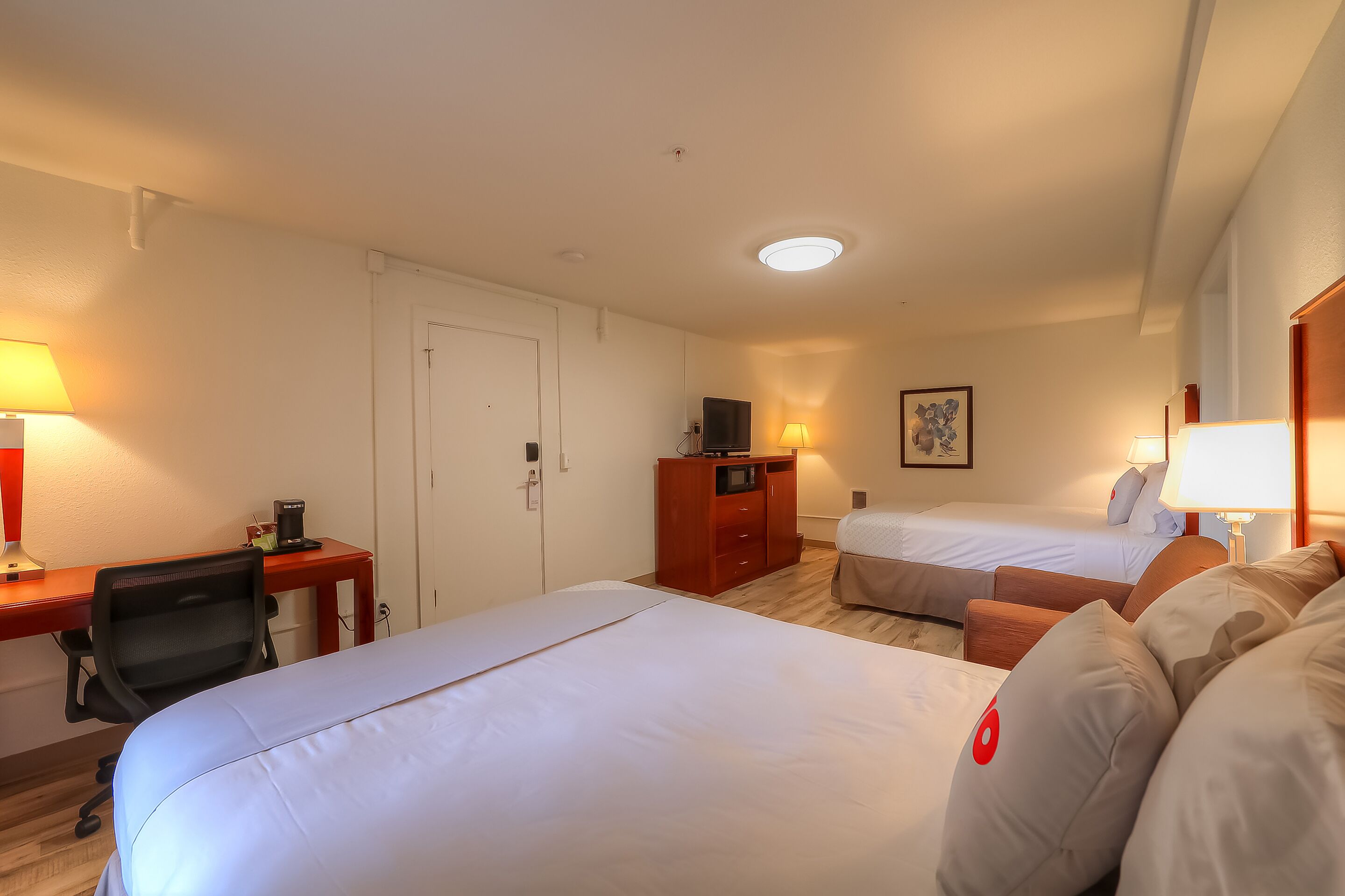 Quarto de hotel com duas camas, uma escrivaninha com cadeira, um guarda-roupa e uma televisão.