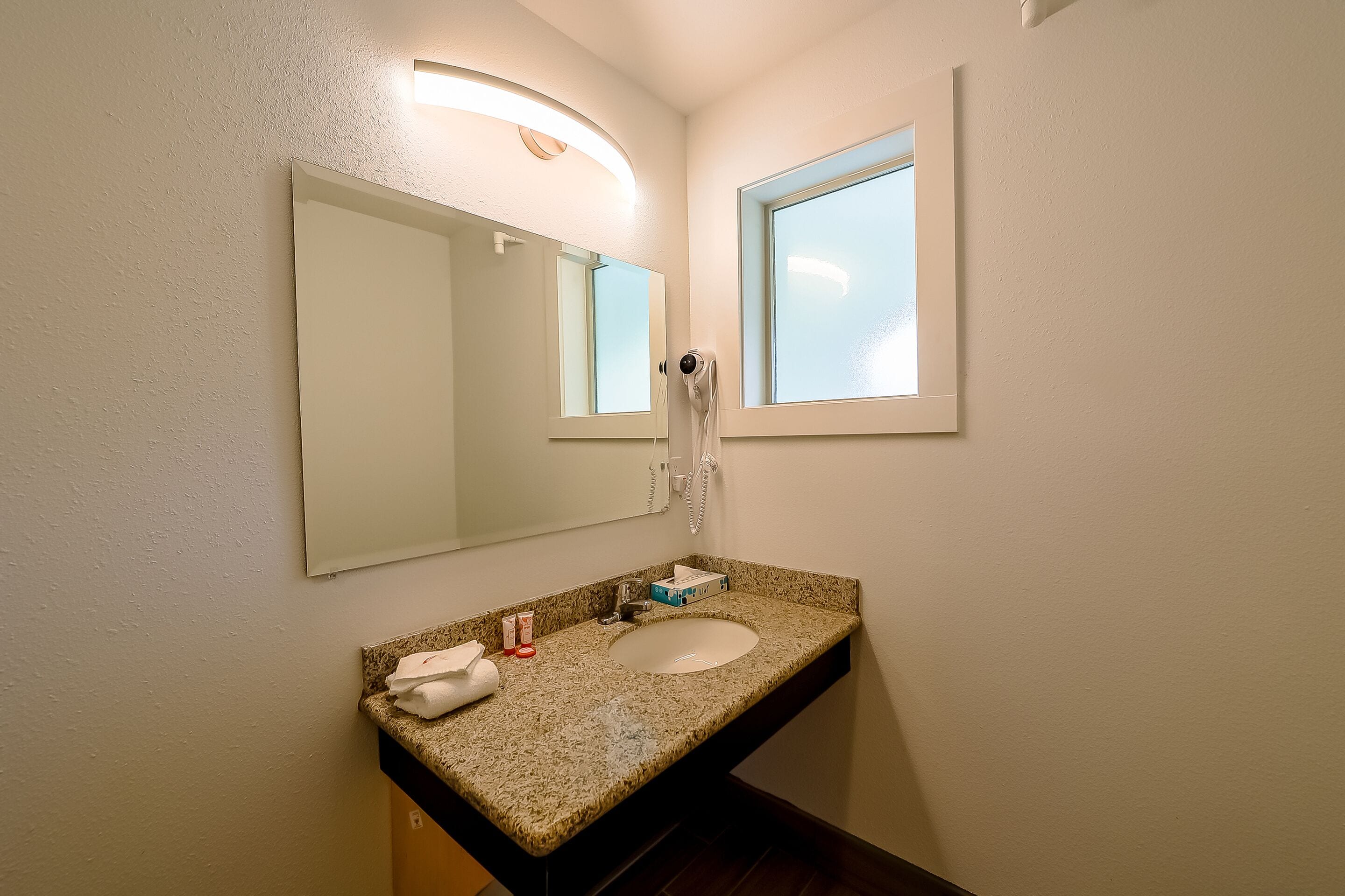 A bathroom with a granite countertop sink, a large mirror, a towel, and a hairdryer.