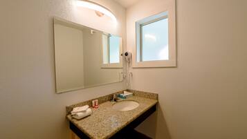A bathroom with a granite countertop sink, a large mirror, a towel, and a hairdryer.