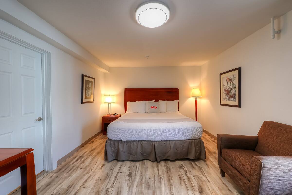Une chambre d’hôtel avec un lit, des lampes de chevet, un plancher en bois, une porte et un tableau encadré au mur.