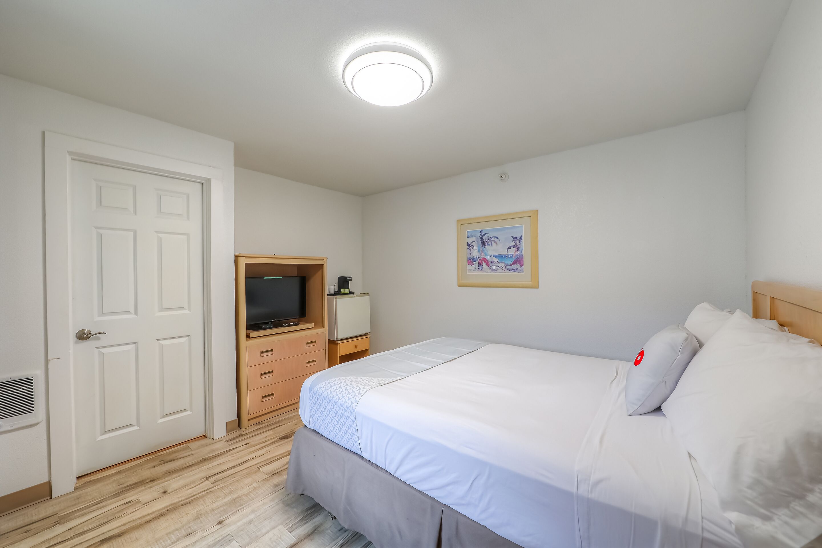 Een slaapkamer met een bed, een televisie, een klein bureau en een schilderij aan de muur.