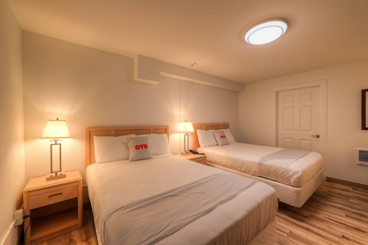 Une chambre d’hôtel avec deux lits, une table de chevet avec une lampe, un plancher en bois et un luminaire au plafond.