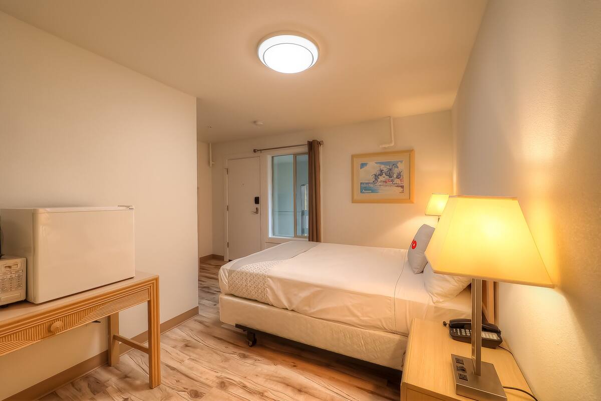 Une chambre d’hôtel avec un lit, une lampe de chevet et une petite table sur laquelle se trouve un réfrigérateur.