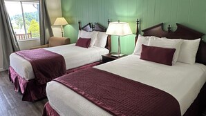 Habitación de hotel con dos camas, paredes verdes, cabeceras de madera y un ventanal con cortinas.