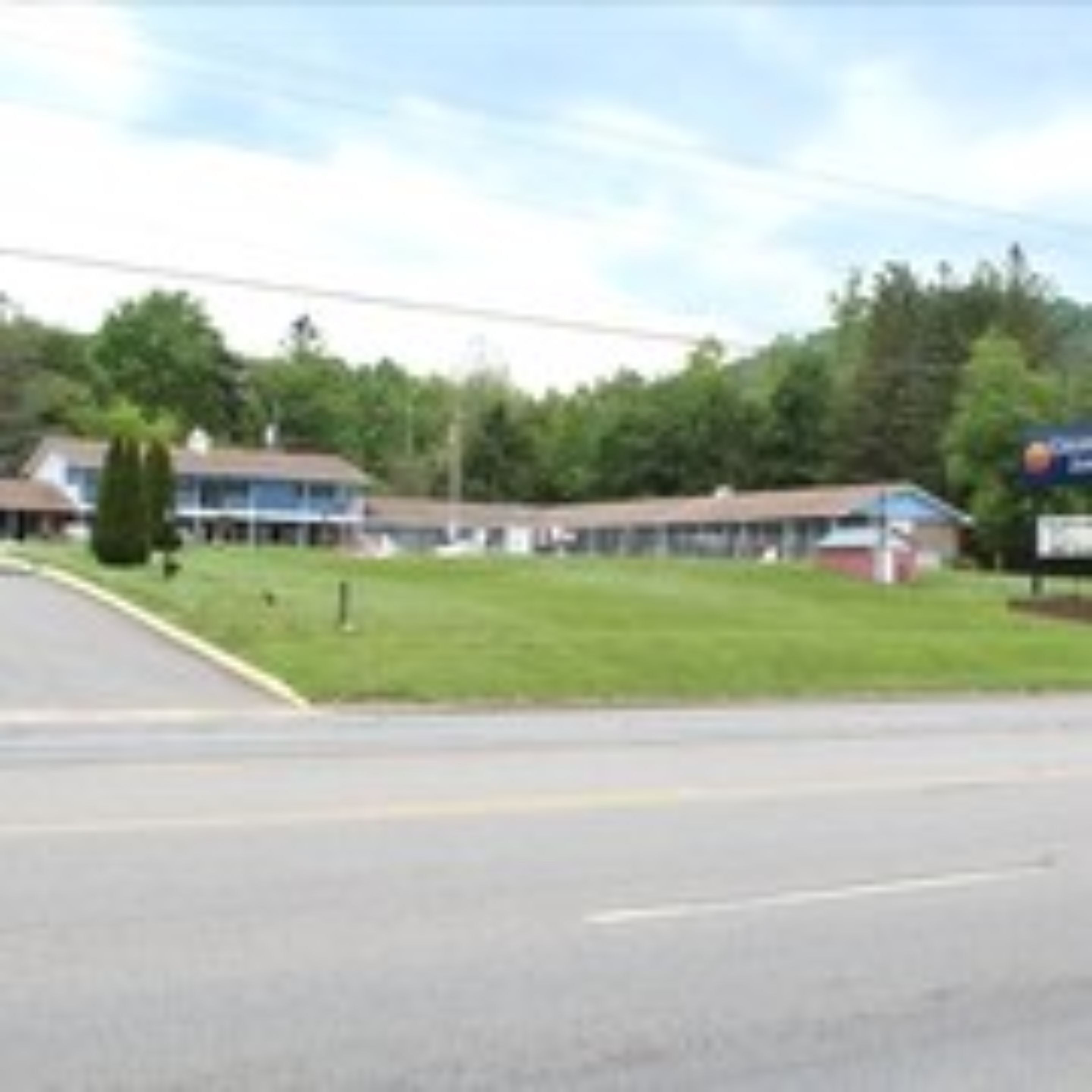 A motel with a large parking lot, a grassy area, and a building with a blue roof.