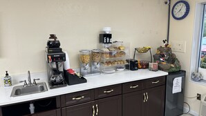 Una kitchenette equipada con cafetera, dosificadores de azúcar y leche, tostadora y una cesta de fruta.