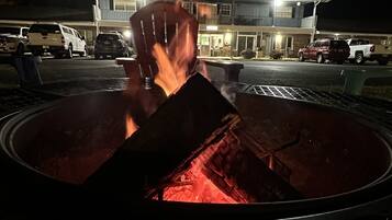 Hoguera con leña ardiendo por la noche, rodeada por una rejilla metálica.