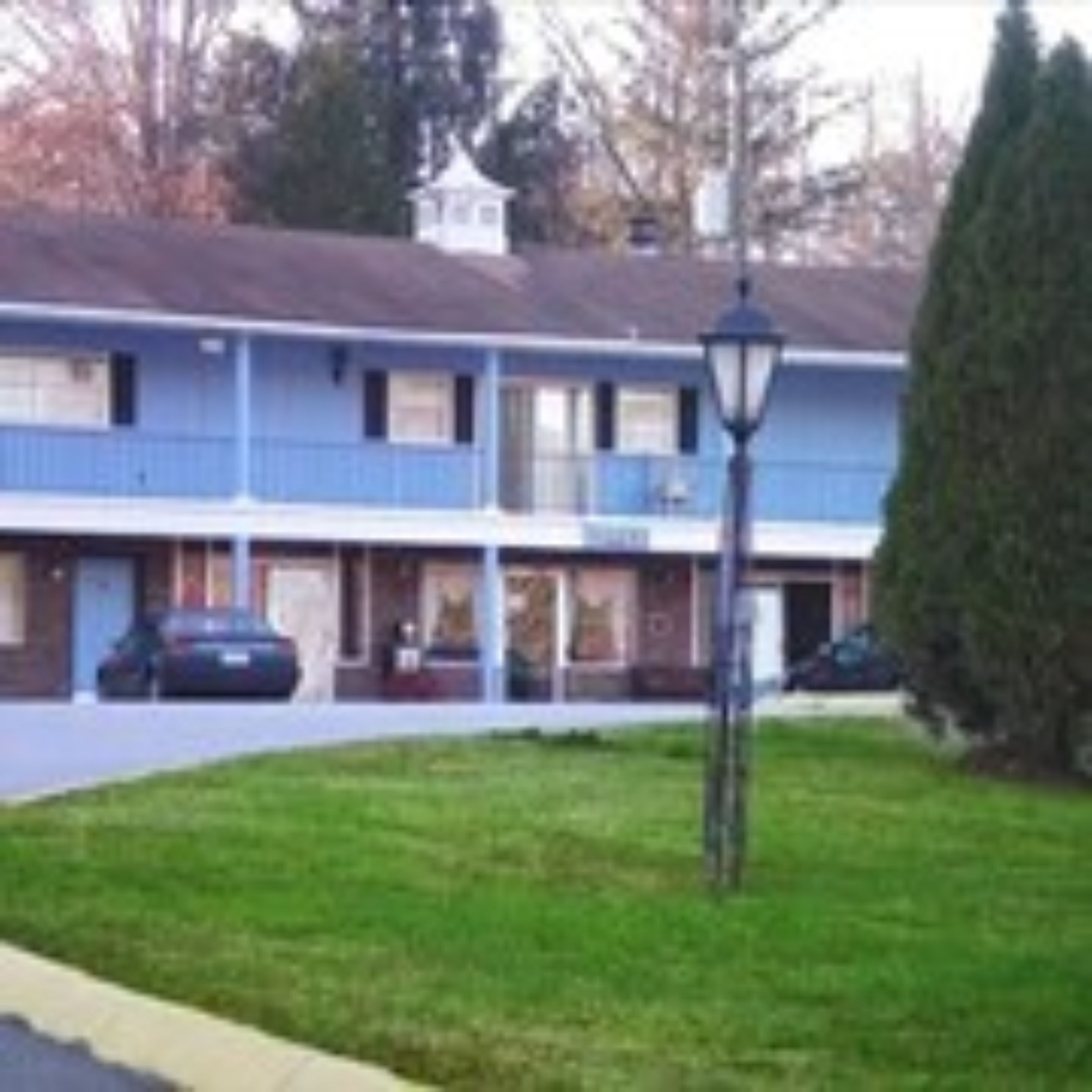 A two-story motel with a central entrance, a small porch, and a parking area.