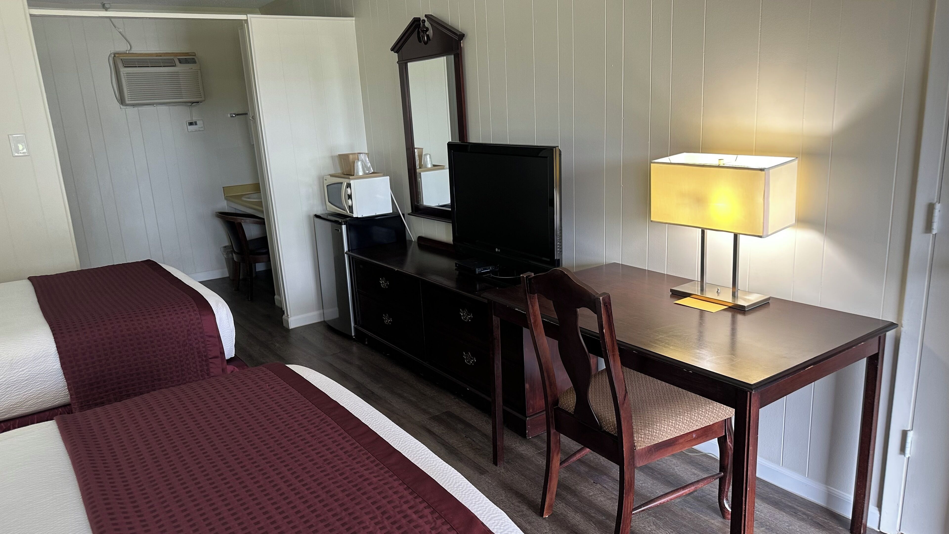A hotel room with a bed, a desk with a TV, a chair, a lamp, a dresser, and a mirror.