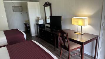 A hotel room with a bed, a desk with a TV, a chair, a lamp, a dresser, and a mirror.
