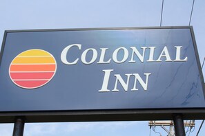 A sign for Colonial Inn with a logo featuring horizontal stripes in yellow, orange, and red.