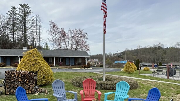 Un brasero rodeado de sillas Adirondack de colores en un entorno exterior, con un asta de bandera y un edificio al fondo.