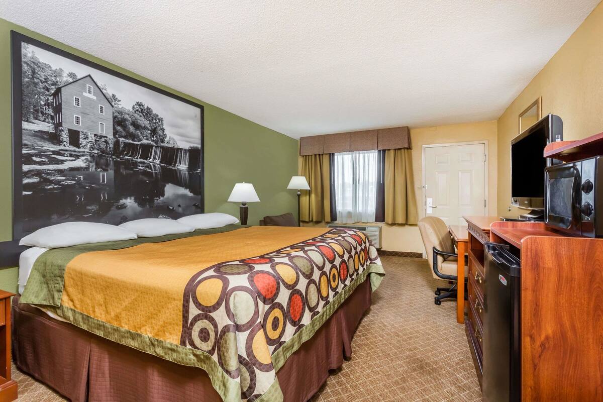 A hotel room with a large bed, a desk with a television, a chair, and a wall-mounted TV.