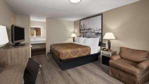 Une chambre d’hôtel comprenant un lit, un bureau avec une télévision, une chaise et une table de chevet avec une lampe.