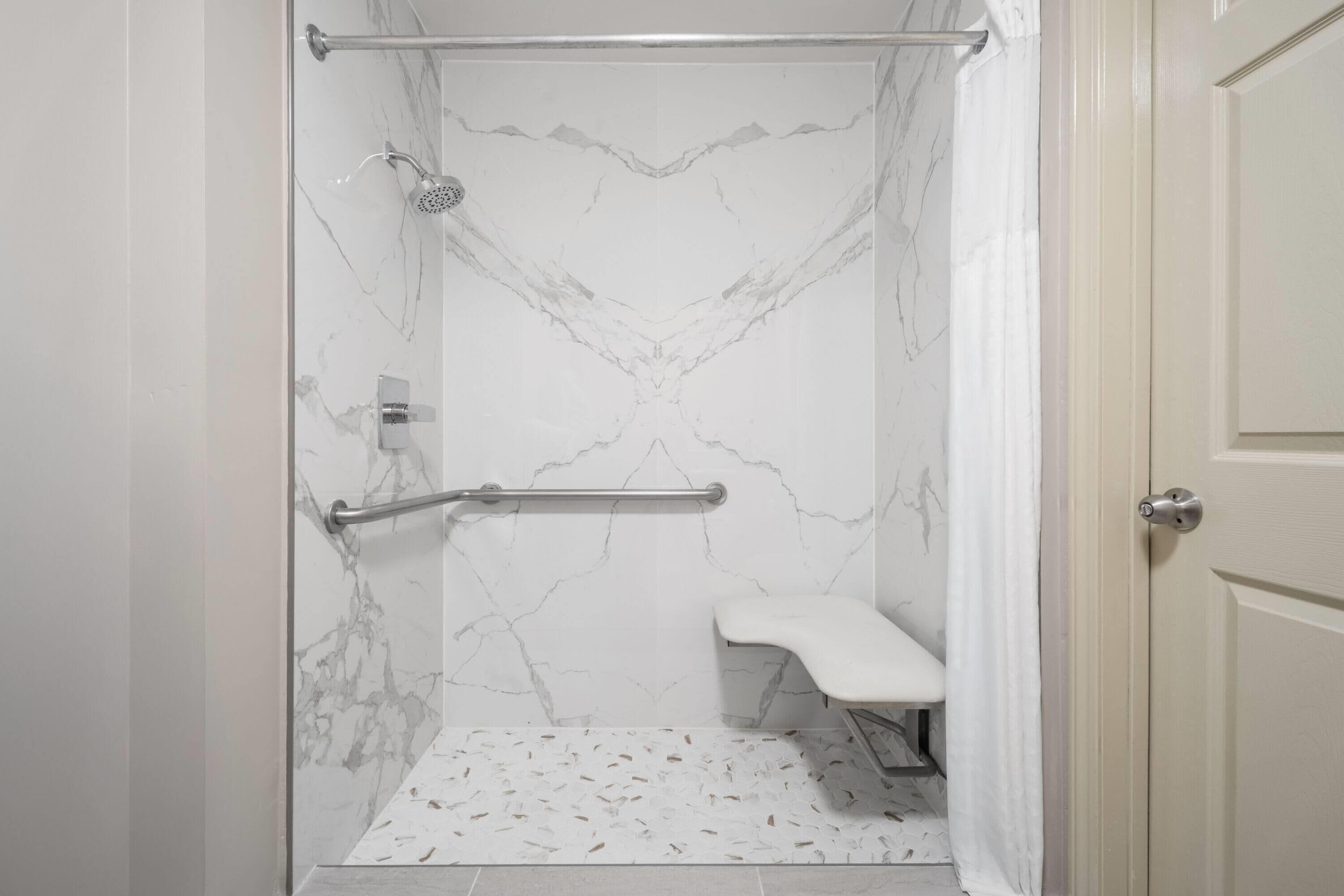 A bathroom with a shower, a handrail, and a bench.