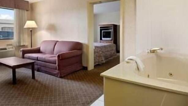 Une chambre d’hôtel avec un canapé, une petite table, une baignoire et un téléviseur dans un coin.