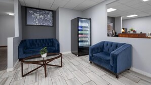 Un hall d’entrée moderne avec un canapé bleu, une table basse, un réfrigérateur rempli de boissons et un comptoir d’accueil.