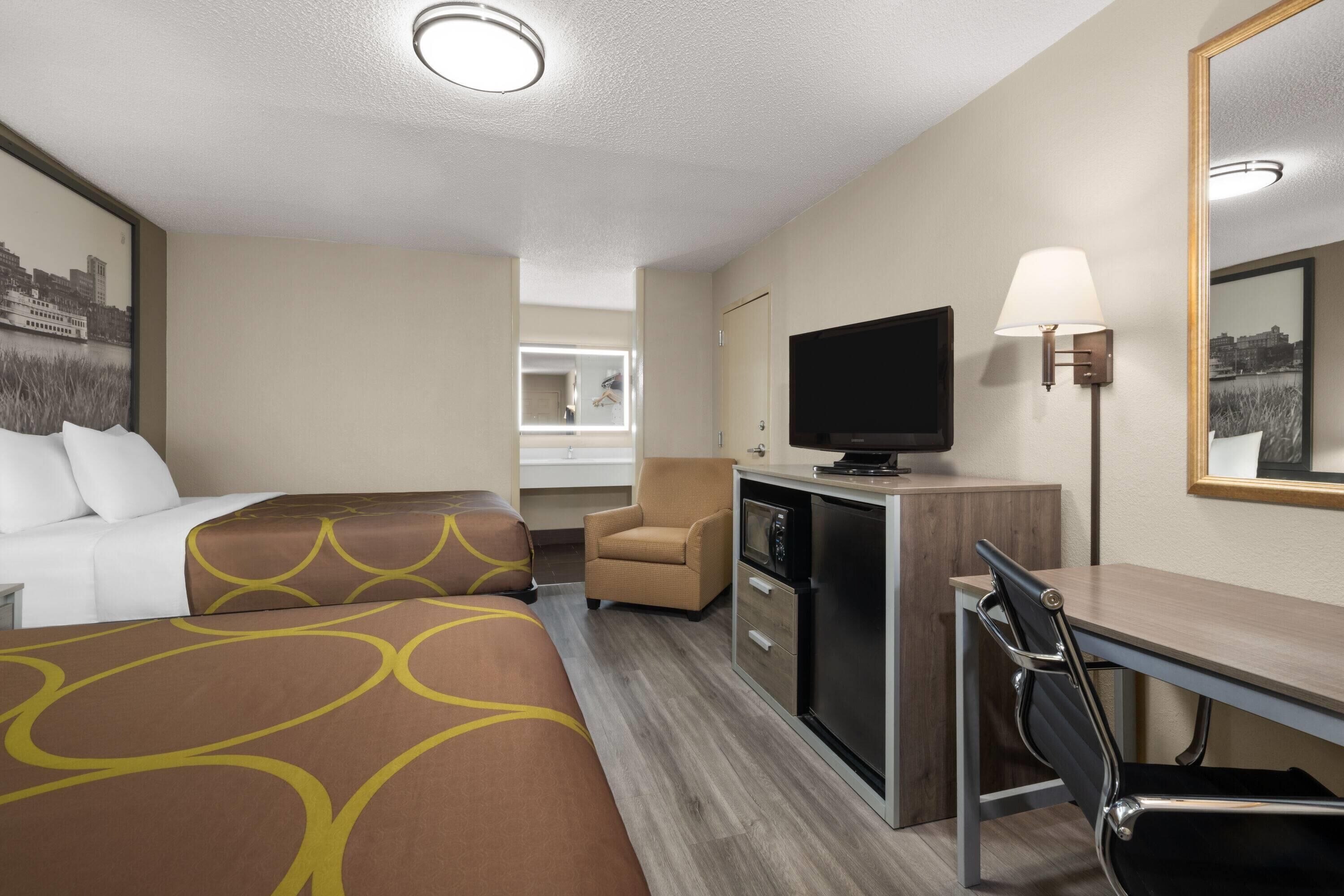 A hotel room with two beds, a desk, a television, a chair, and a mirror.