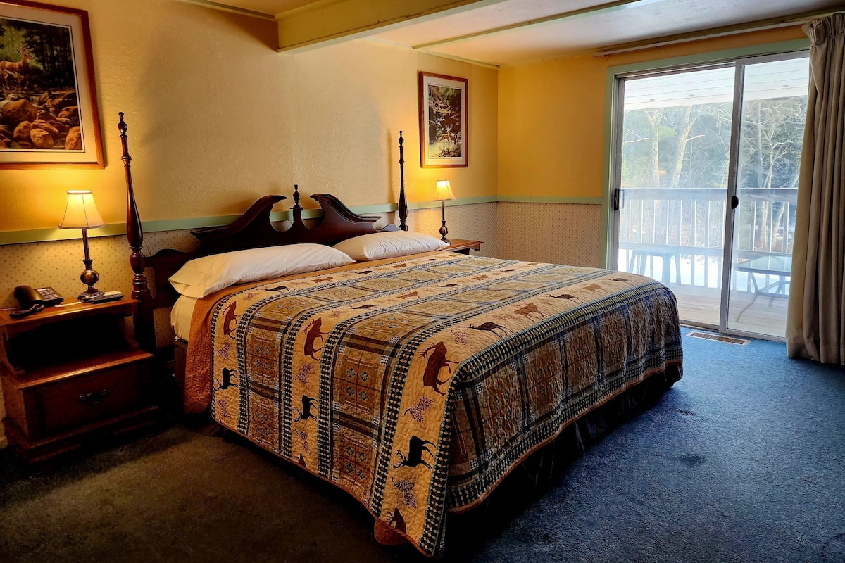 A bedroom with a large bed, two bedside lamps, a nightstand, and a dresser. There are two framed pictures on the wall.