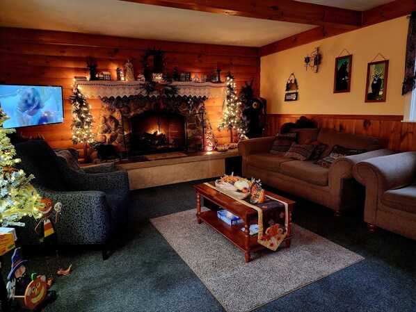 A cozy living room with a fireplace, a television, and a Christmas tree. - Covered Bridge Riverview Lodge (Jackson)