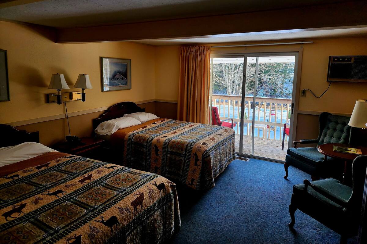A hotel room with two beds, a balcony, a chair, and a TV.