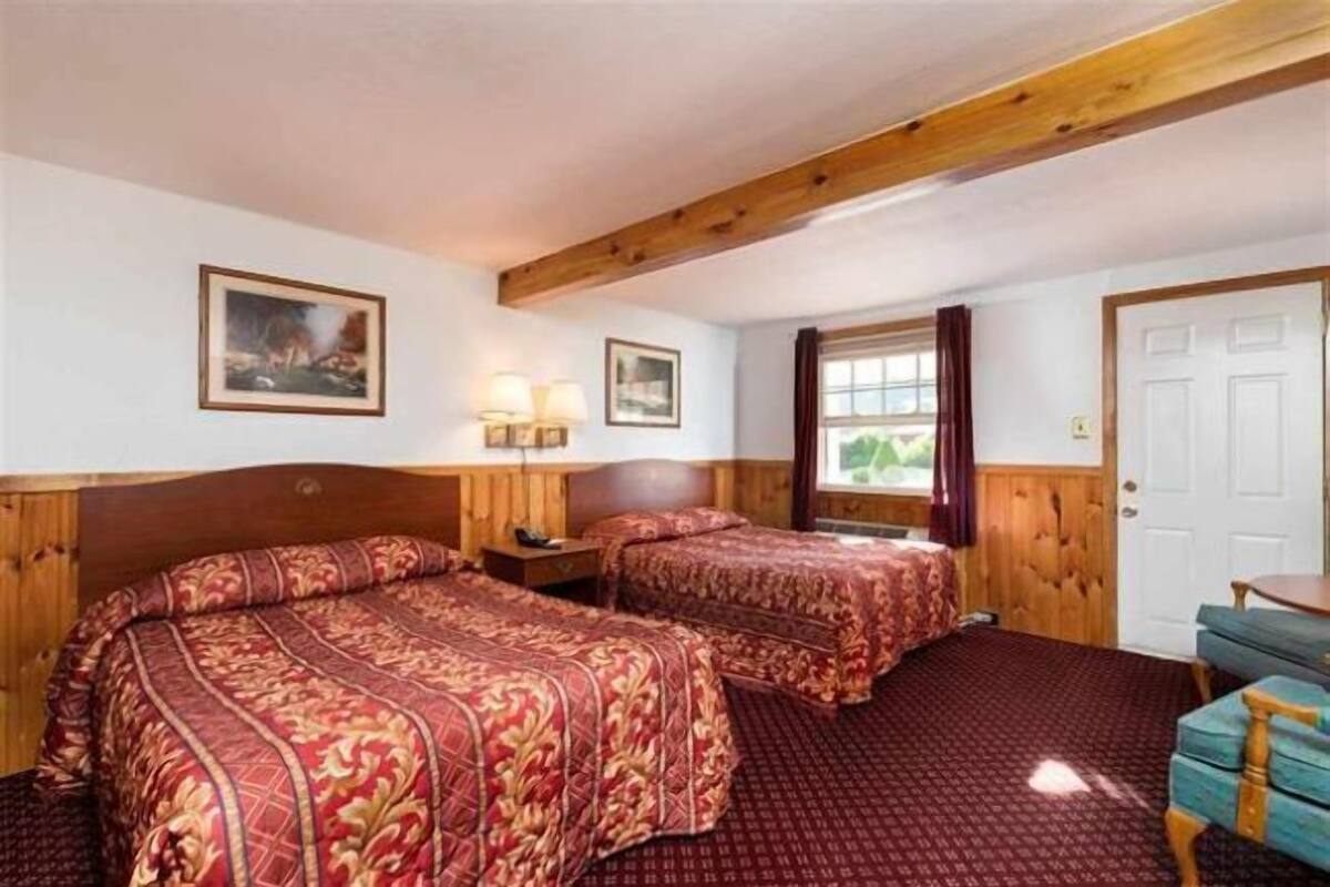 A hotel room with two beds, wooden headboards, a window with curtains, and a door.