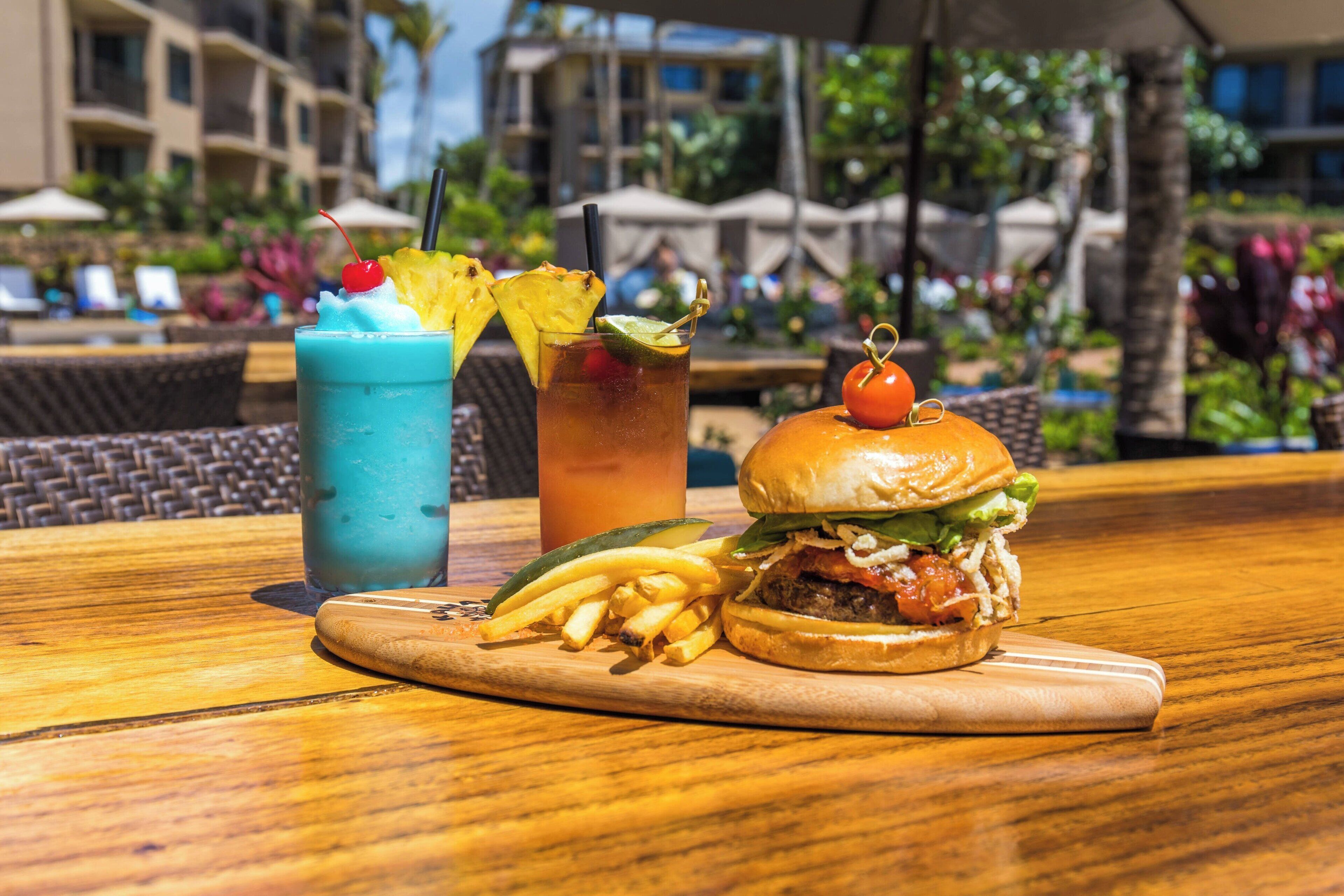 A meal with a burger, fries, and two drinks on a wooden table.