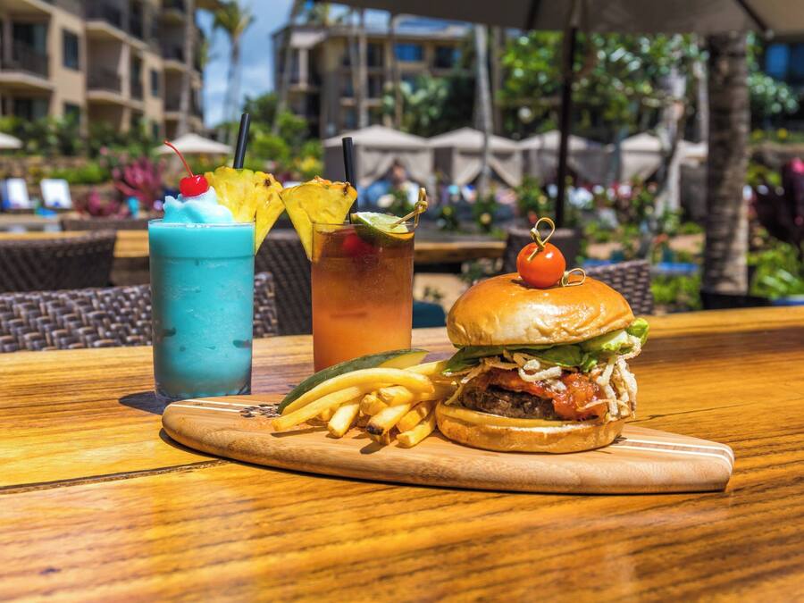 Un repas composé d’un hamburger, de frites et de deux boissons, servi sur une table en bois.