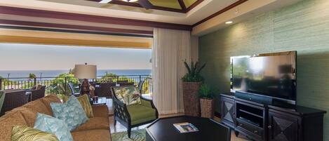A spacious living area with a large flat-screen TV, comfortable seating, and a view of the ocean.