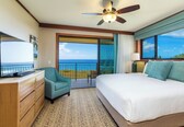 A hotel room with a large bed, a television, a desk, a chair, and a balcony with a view of the ocean.