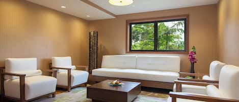 A modern living room with a white sofa, two armchairs, a coffee table, and a large window with a view of greenery.
