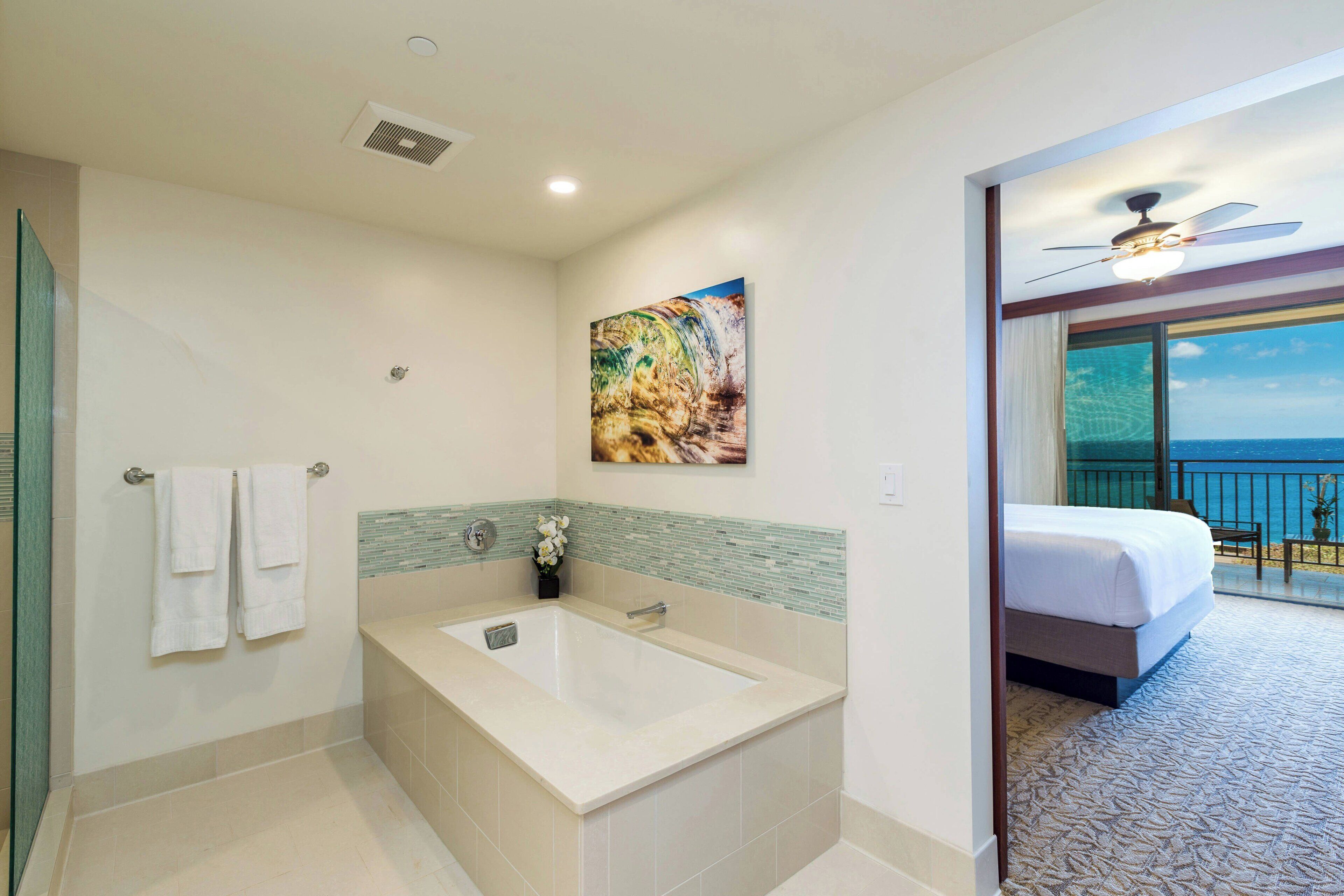 A modern bathroom with a bathtub, a shower, and a large window offering a view of the ocean.