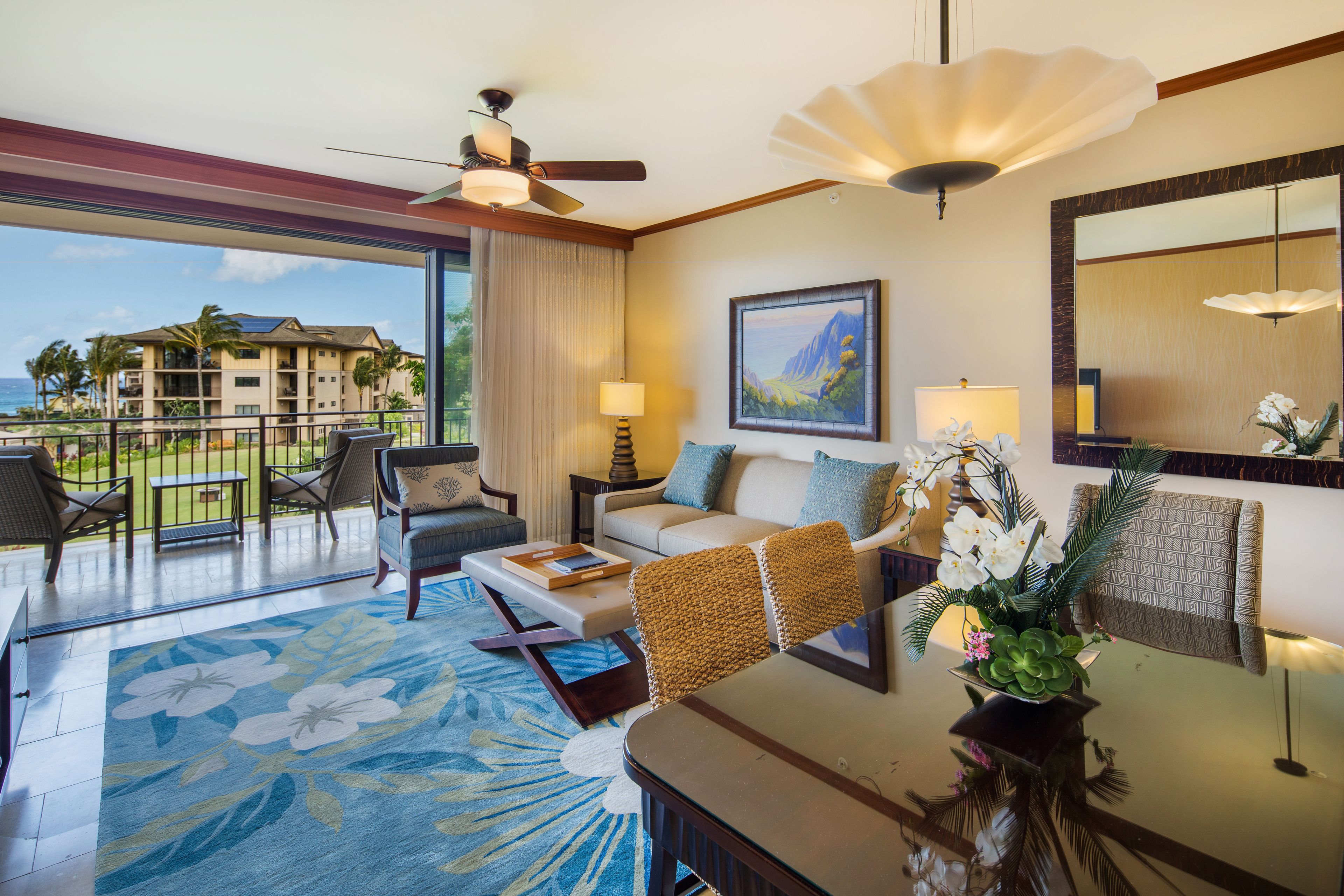 A hotel room with a balcony, a ceiling fan, a sofa, a coffee table, and a dining table.