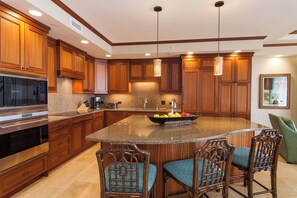 A kitchen with wooden cabinets, a granite countertop, a built-in microwave, and a large island with bar stools.