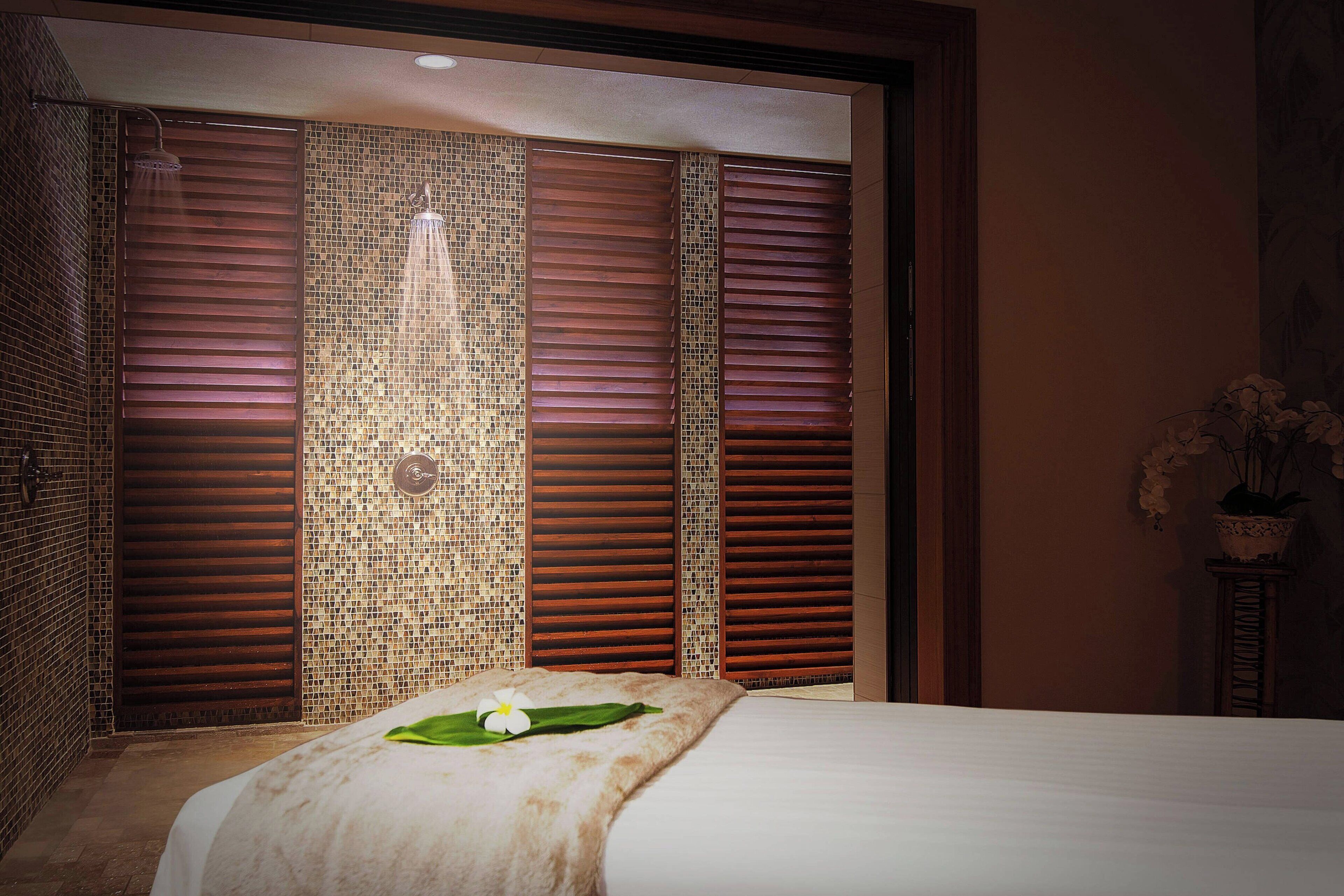 A hotel room with a bed, a shower area with sliding doors, and a decorative wall with a mosaic pattern.