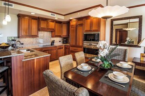 A modern kitchen with wooden cabinets, granite countertops, and a dining area with a large island and patterned chairs.