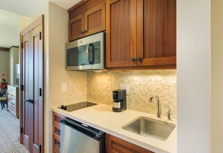 A kitchen with wooden cabinets, a stainless steel dishwasher, a coffee maker, and a tiled backsplash.