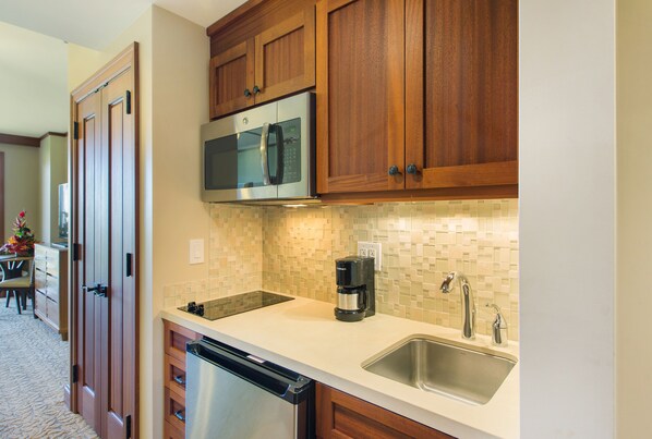 A kitchen with wooden cabinets, a stainless steel dishwasher, a coffee maker, and a tiled backsplash.