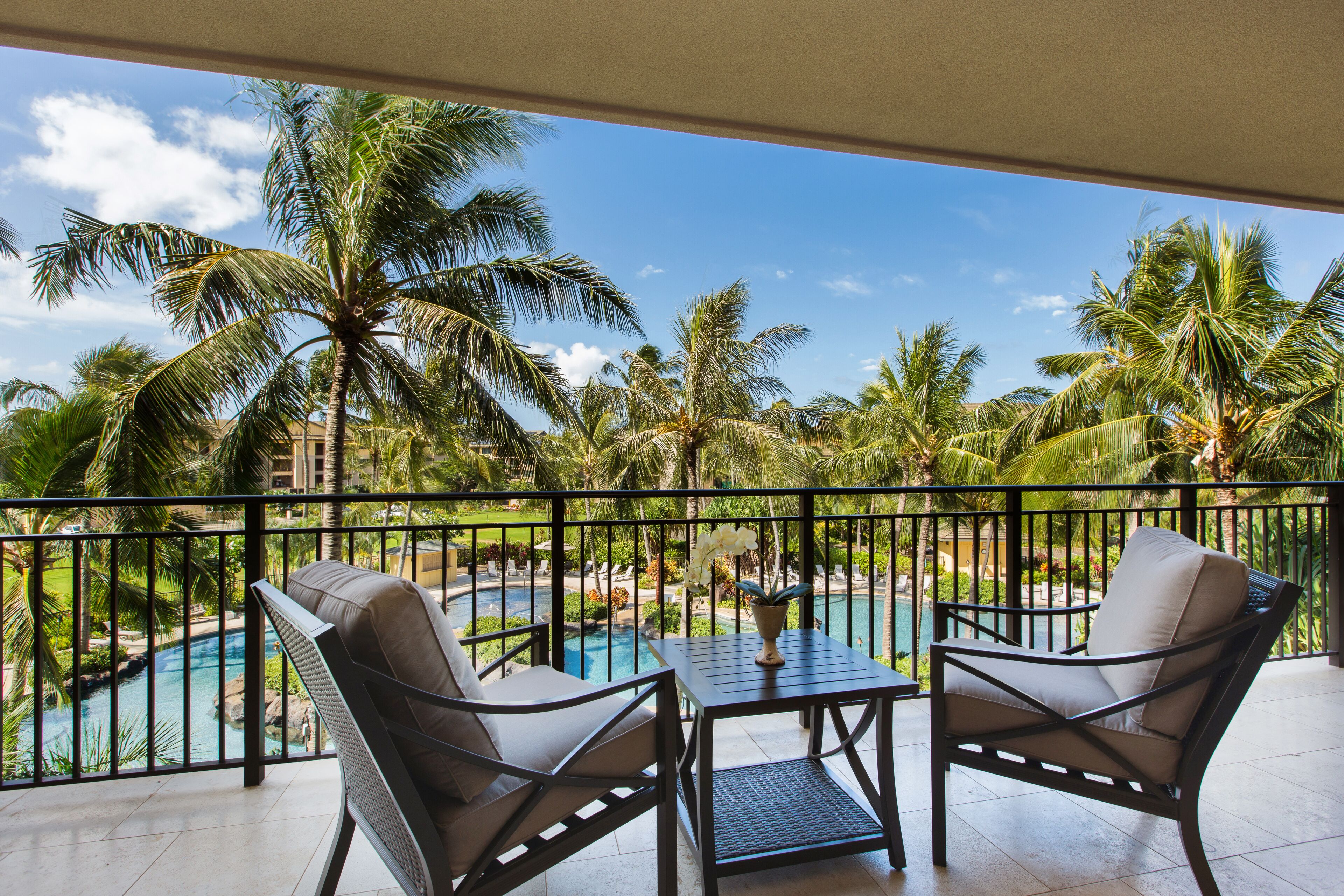 Un balcon avec deux chaises, une table et une vue sur une piscine entourée de palmiers.